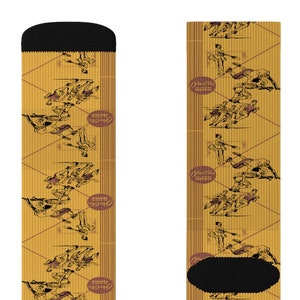 May include: A pair of socks with a repeating pattern of figures in brown on a yellow background. The socks have black toes and heels, and the figures are interspersed with oval text labels.