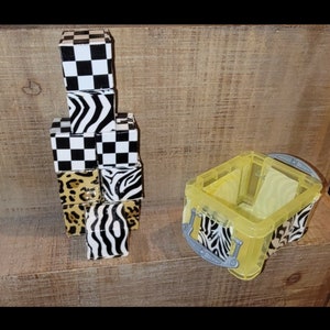 May include: A set of small, colorful boxes with different animal print designs, including zebra, leopard, and checkered patterns. The boxes are stacked on top of each other and are made of a clear plastic material.