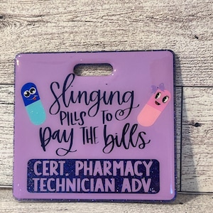 Puede incluir: Una placa morada con un recorte para el asa, con el texto "Slinging Pills to Pay the Bills". La placa incluye gráficos de pastillas de dibujos animados y el texto "CERT. PHARMACY TECHNICIAN ADV." en una fuente brillante.