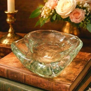 May include: A clear glass bowl with an irregular, organic shape and a thick, rippled texture. The bowl features a wide, open top and a deep, uneven basin, showcasing a transparent appearance that reflects light across its wavy, moulded surface.