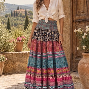 May include: A long, tiered maxi skirt featuring a high, smocked waistband and a vibrant, multi-colored pattern of floral and geometric prints in shades of blue, pink, red, and yellow, finished with a black and white patterned hemline.