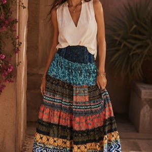 May include: A sleeveless cream-colored V-neck top paired with a long, tiered maxi skirt featuring a patchwork design of various patterns and colors, including blue, orange, yellow, and black, with a wide, smocked elastic waistband.