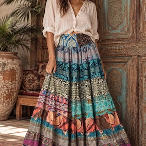 May include: A long, tiered skirt featuring a patchwork of various colorful patterns in shades of blue, teal, pink, and purple. The skirt has a high-waisted fit and a full, flowing silhouette that reaches the ankles, paired with a light beige button-down shirt.