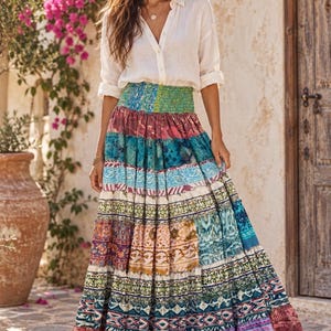 May include: A long, tiered maxi skirt featuring a vibrant patchwork of multicolored patterns in shades of blue, pink, green, and purple, paired with a white button-down shirt with long sleeves and a collared neckline, and brown strappy sandals.