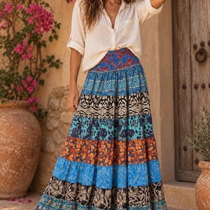 May include: A long, tiered maxi skirt featuring a vibrant patchwork of horizontal bands in various patterns and colors, including blue, orange, black, and white, paired with a light beige, long-sleeved button-down shirt with a single chest pocket.
