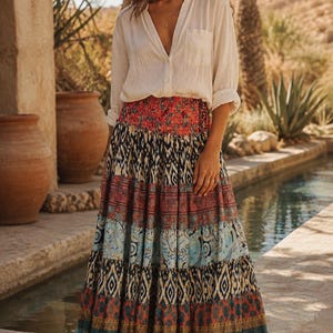 May include: A long-sleeved white button-down shirt with a collar and a chest pocket paired with a floor-length tiered maxi skirt featuring a multi-colored patchwork pattern of floral, geometric, and paisley prints in shades of red, blue, and tan.