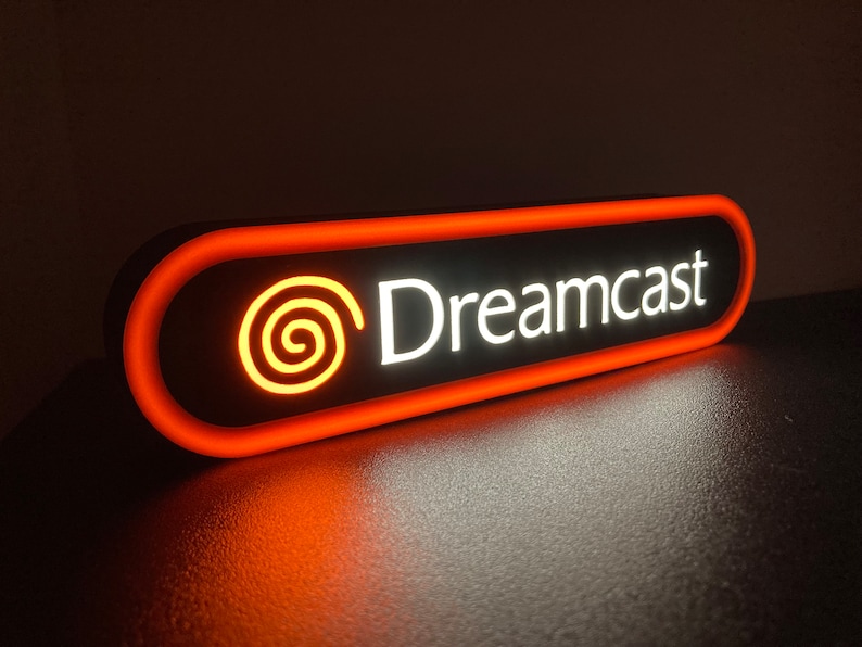 May include: A black and orange neon sign with the text "Dreamcast" and a stylized orange swirl logo.