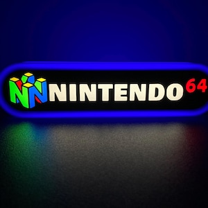 Puede incluir: Un letrero rectangular azul y negro con un logotipo "NINTENDO 64" blanco y un logotipo de Nintendo 64 colorido en el lado izquierdo.