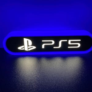 May include: A white and blue illuminated sign with the PlayStation logo and the text "PS5" in white.