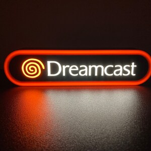 May include: A red and white illuminated sign with the text "Dreamcast" and a stylized orange swirl logo.