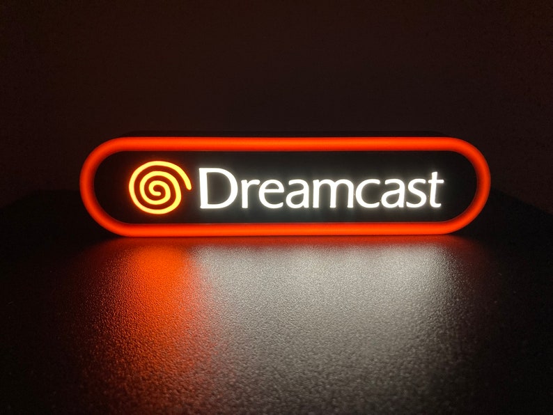 May include: A red and white illuminated sign with the text "Dreamcast" and a stylized orange swirl logo.
