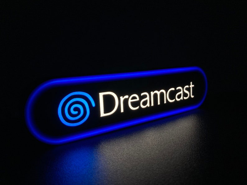 May include: A blue and white illuminated sign with the text "Dreamcast" and a stylized blue swirl logo.