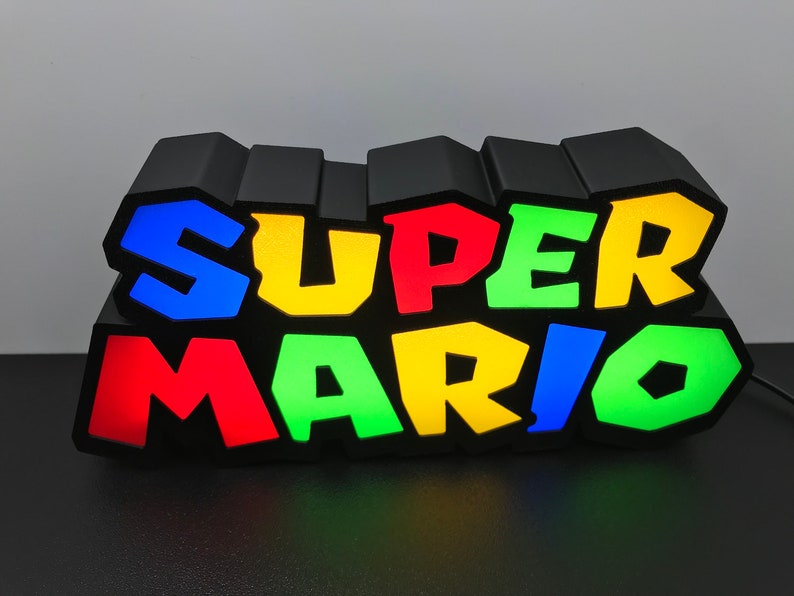 May include: A black light-up sign with the words "SUPER MARIO" in colorful 3D letters. The letters are blue, yellow, green, and red.