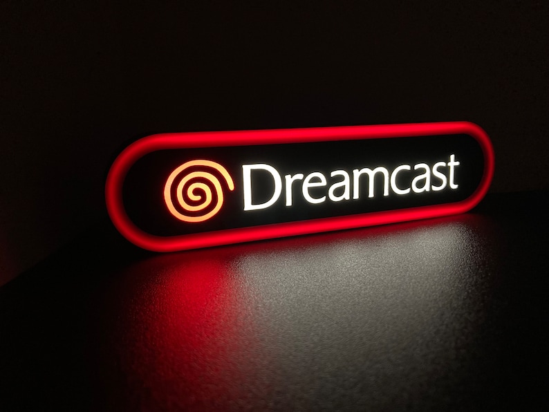 May include: A red and white neon sign with the text "Dreamcast" and a stylized logo of a red swirl.