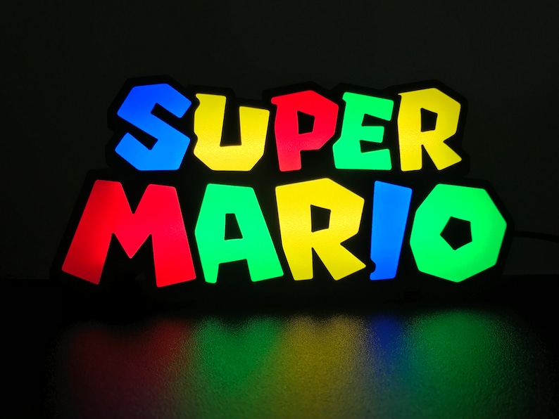 May include: A colorful light-up sign that reads "SUPER MARIO" in a retro video game style. The letters are outlined in black and each letter is a different color: blue, yellow, red, green, and blue.