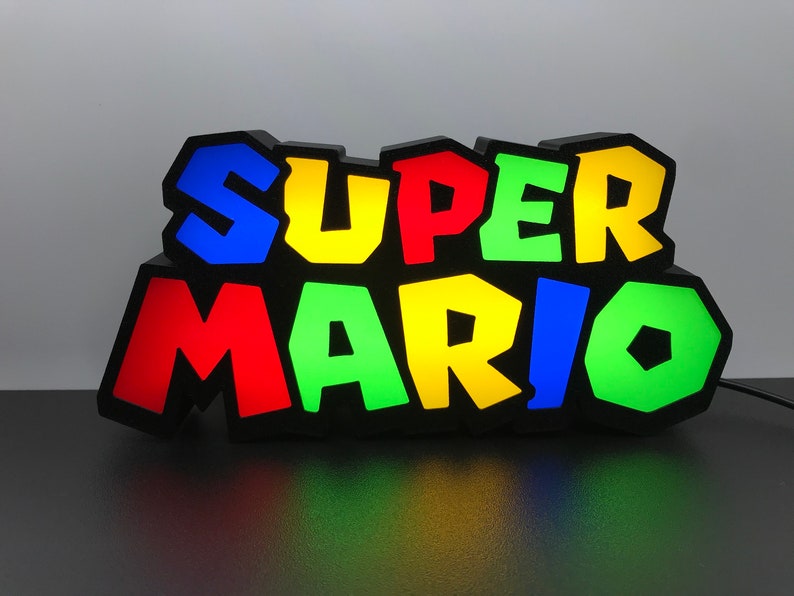 May include: A black light-up sign with the words "SUPER MARIO" in colorful, blocky letters. The letters are lit up in different colors: blue, yellow, green, and red.
