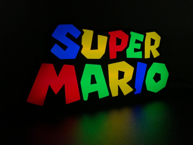 May include: A colorful, illuminated sign with the words "SUPER MARIO" in a retro video game style font. The letters are outlined in black and each letter is a different color: blue, yellow, red, green, yellow, blue, green.