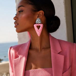 Pode incluir: Um brinco de destaque com uma peça superior semicircular com riscas de zebra a preto e branco, ligada a um grande pendente triangular cor-de-rosa com efeito marmoreado. O brinco é usado no lóbulo e apresenta um design geométrico.