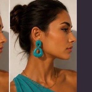 May include: A pair of teal drop earrings featuring two connected, smooth, rounded geometric shapes. The earrings have a glossy finish and are worn with a matching teal one-shoulder top and a thin gold-toned chain necklace. The word TEAL is printed below.
