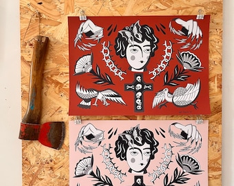 May include: Two tattoo-style art prints, one red and one pink, featuring a woman's face, cross, skulls, birds, and other elements. The prints are clipped to a wooden board, with an axe on the left side.