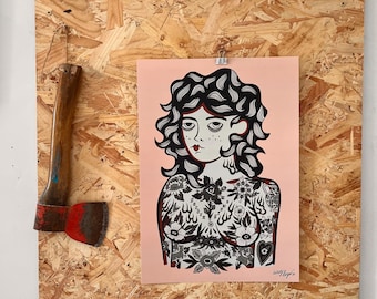 May include: A pink print of a woman with black curly hair and floral tattoos, mounted on a wood board. An axe with a wooden handle and red blade is mounted on the board. The artwork is signed.