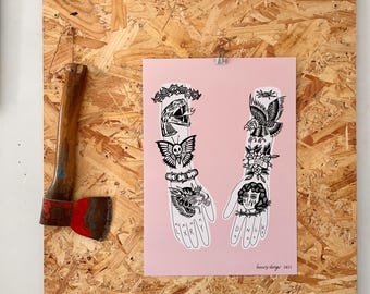 May include: A pink print featuring two stylized hands with tattoo designs, including a snake, eagle, and skull. The print is attached to a wooden board with a small axe on the side. The text "luxury danger 2023" is visible.