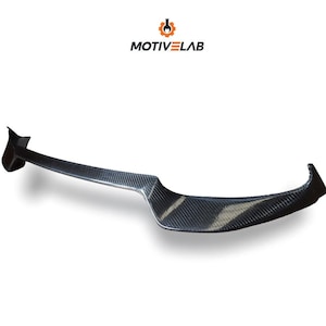 Puede incluir: Un difusor trasero de fibra de carbono negro para un coche. El difusor tiene una forma curva y una superficie texturizada.