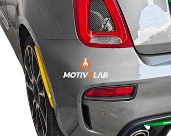 Può includere: Sezione posteriore di un'auto grigia con fanale posteriore rosso e accento giallo. L'auto ha una ruota nera e uno scarico cromato. Il testo "MOTIV LAB" è visibile.