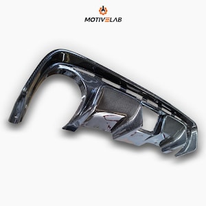 Peut inclure: Un diffuseur arrière en fibre de carbone noire pour une voiture. Le diffuseur présente un motif en nid d'abeille et un design élégant.