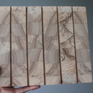 May include: A close-up of a light brown wood panel with a unique grain pattern. The panel is made up of several smaller pieces of wood that have been joined together to create a larger, more stable piece.