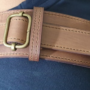 May include: A brown leather belt with a brass buckle. The belt is double layered and has stitching along the edges.