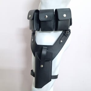 May include: A black leather utility belt featuring three rectangular pouches with silver-tone snap closures attached to the waist, connected to a drop-leg holster with a vertical strap and a single snap button, secured by an adjustable thigh strap.