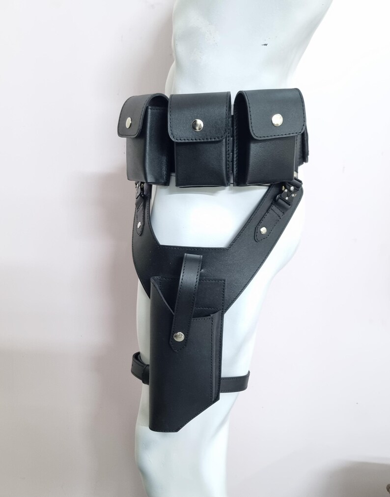 May include: A black leather utility belt featuring three rectangular pouches with silver-tone snap closures attached to the waist, connected to a drop-leg holster with a vertical strap and a single snap button, secured by an adjustable thigh strap.