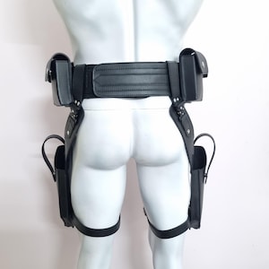 May include: A black tactical utility belt system featuring a wide waist strap with horizontal stitching, two top-mounted pouches, and two lower leg-mounted holsters connected by vertical straps and adjustable thigh bands with metal hardware.