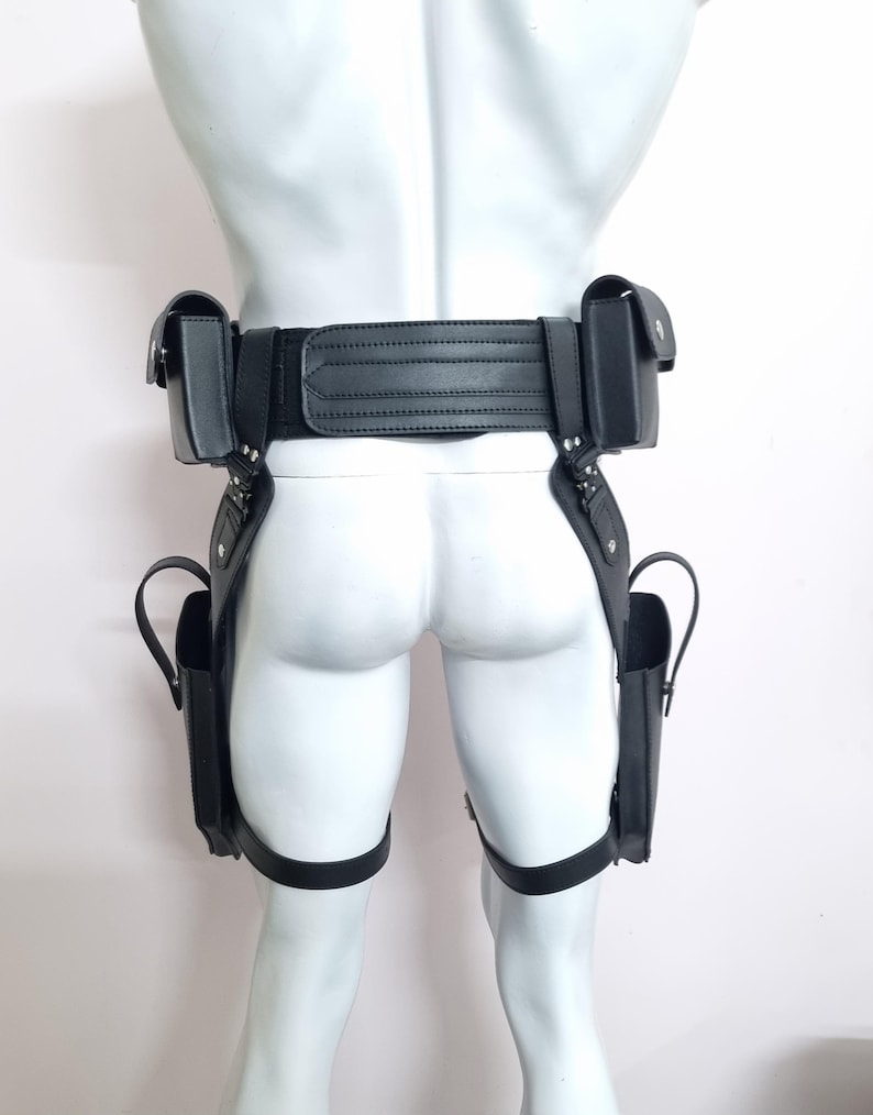 May include: A black tactical utility belt system featuring a wide waist strap with horizontal stitching, two top-mounted pouches, and two lower leg-mounted holsters connected by vertical straps and adjustable thigh bands with metal hardware.