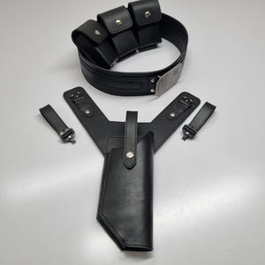 May include: A black leather utility belt featuring three attached pouches with silver-tone snap closures and a metallic buckle, accompanied by a matching black leather holster assembly with two separate straps and silver-tone hardware accents.