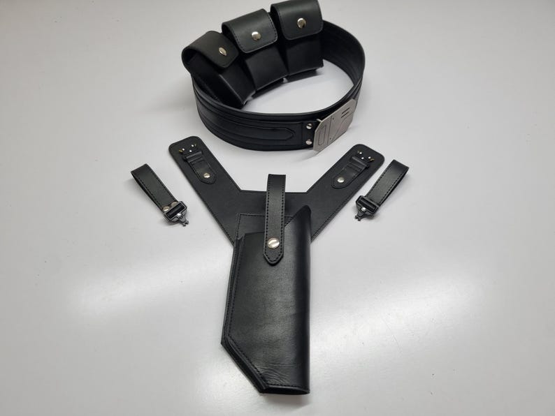 May include: A black leather utility belt featuring three attached pouches with silver-tone snap closures and a metallic buckle, accompanied by a matching black leather holster assembly with two separate straps and silver-tone hardware accents.