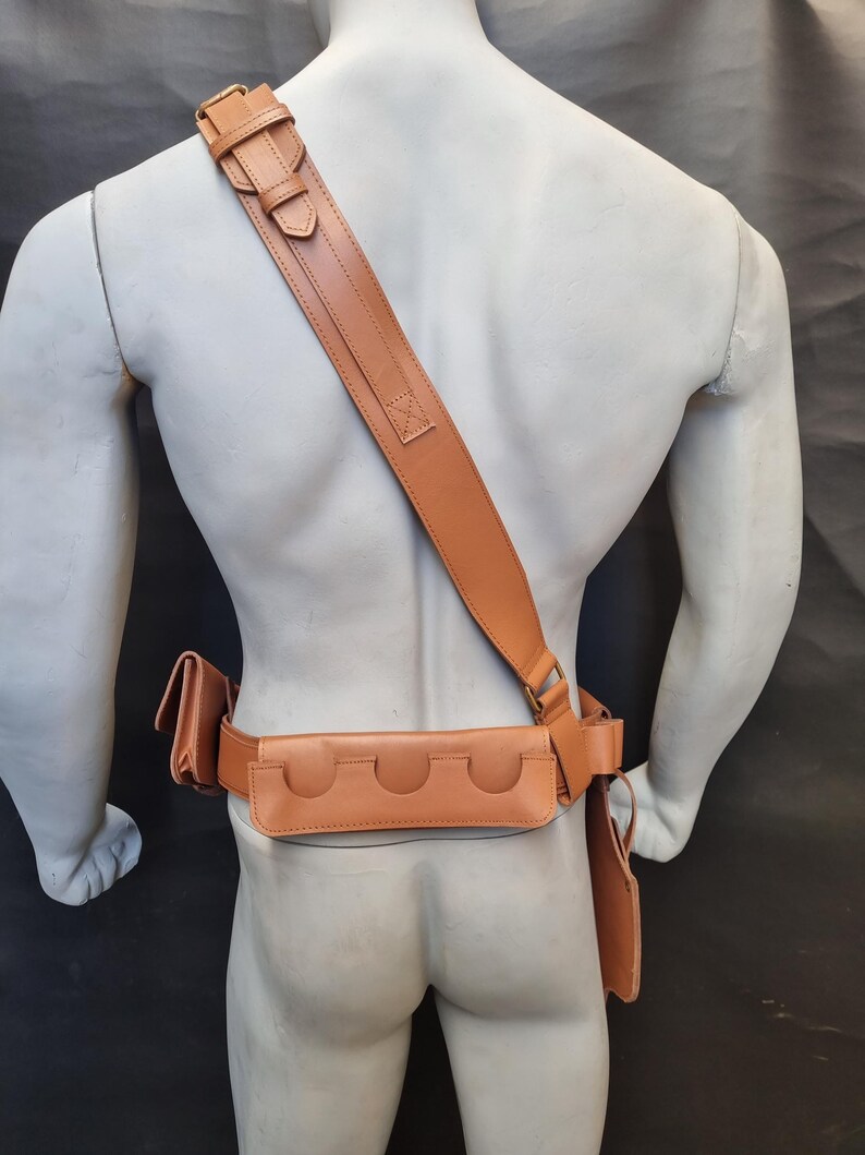 May include: A brown leather belt with a holster and a shoulder strap. The belt has multiple pouches and a buckle.