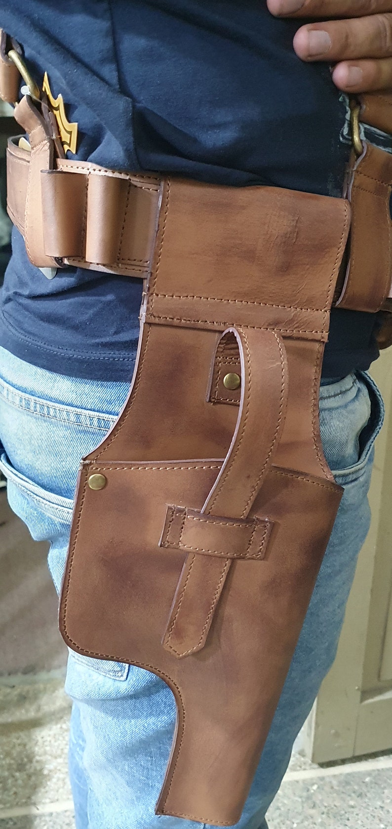 May include: A brown leather holster with a strap and a metal button. The holster is worn on a person's hip.