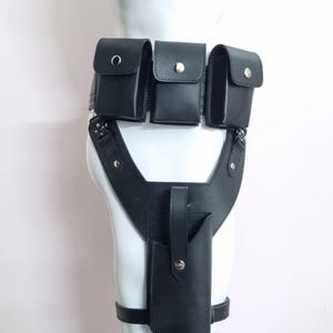 May include: A black leather utility belt featuring three rectangular pouches with silver-tone snap closures attached to the waist, connected to a vertical holster with a strap and snap button, secured by a leg strap around the thigh.