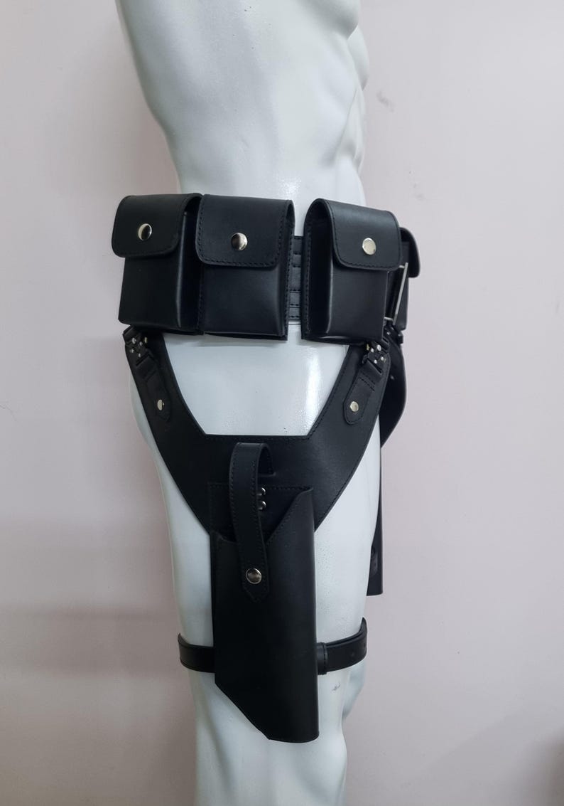 May include: A black utility belt featuring three rectangular pouches with silver snap closures attached to the waist, connected to a vertical holster on the thigh with a matching silver snap, all constructed from a smooth, matte black material.