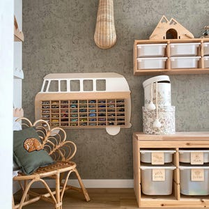 May include: A wall-mounted wooden toy car display case shaped like a vintage van, a rattan chair with a green deer pillow, a wooden storage unit with white bins, a wicker giraffe head wall decor, and stacked round patterned storage boxes.