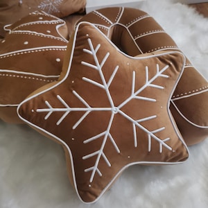 May include: A set of brown velvet cushion covers with white embroidered snowflake designs. The cushions are shaped like a star, a gingerbread man, and a candy cane.