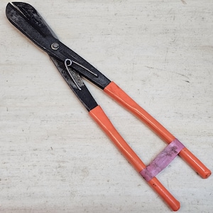 Può includere: Tronchese nero e arancione per impieghi gravosi. Le lame di taglio sono nere e le maniglie sono arancioni con una fascia rosa vicino al centro. Lo strumento è progettato per tagliare materiali spessi.