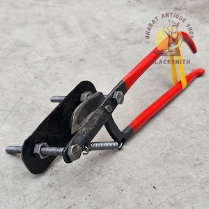 May include: A red and black metal tool with a spring and a blade. The tool is labelled "Bharat Antique Shop Blacksmith".