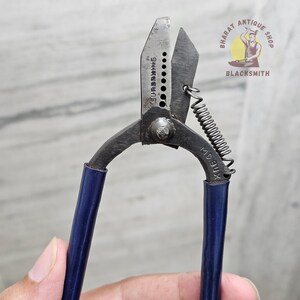以下が含まれることがあります： 青いハンドルが付いたヴィンテージの金属製ハサミ。ハサミにはバネが付いており、刃には「SUPERB KING」の文字が見えます。ハサミは明るい灰色の背景の前に保持されています。