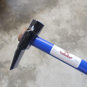 May include: A blue and black pick hammer with a wooden handle. The hammer has a blue handle and a black head. The text "Bharat Antique Shop" is visible on the handle.