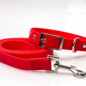 May include: A red rubber dog collar and lead set. The collar has a silver buckle and a silver D-ring. The lead has a silver clip.