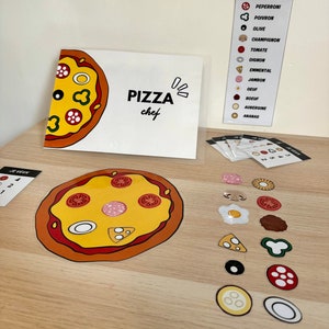 Op de afbeelding: Een pizza-chefspel met een witte kaart waarop "PIZZA chef" staat en een cartoonpizza. Er zijn verschillende kleurrijke stickers met pizzatoppings, waaronder pepperoni, champignons, olijven en tomaten.