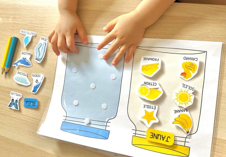 May include: A learning activity for children featuring two jars, one labelled "Blue" and the other "Yellow".  The jars are empty and there are various blue and yellow images to be sorted into the correct jar.  The blue images include a butterfly, a whale, a bird, a water drop, a pair of jeans, and a pool.  The yellow images include a banana, a star, a lemon, a sun, a duck, and a piece of cheese.